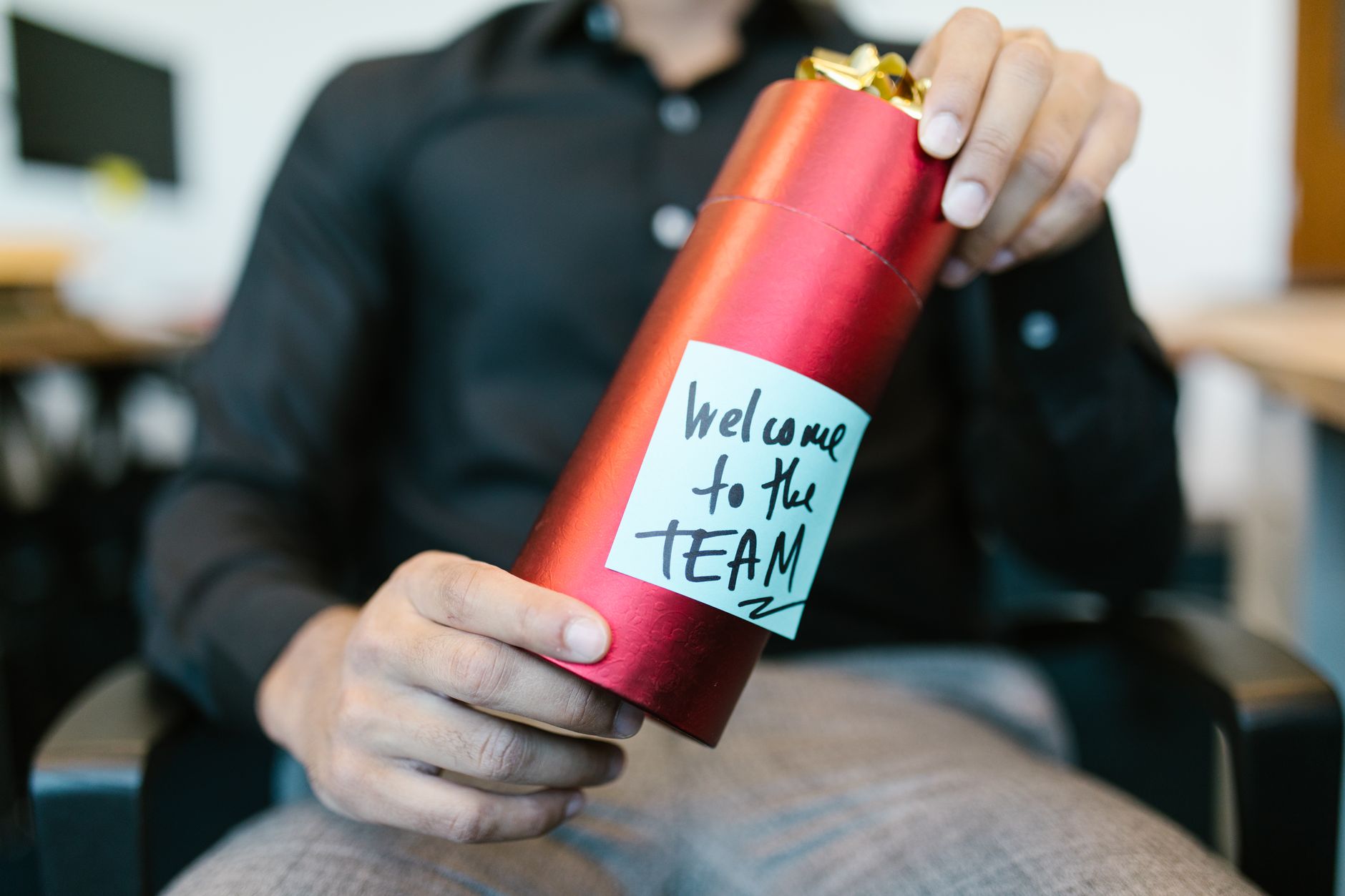 Personne tenant un coffret cadeau rouge accompagné d'un mot de bienvenue dans l'équipe